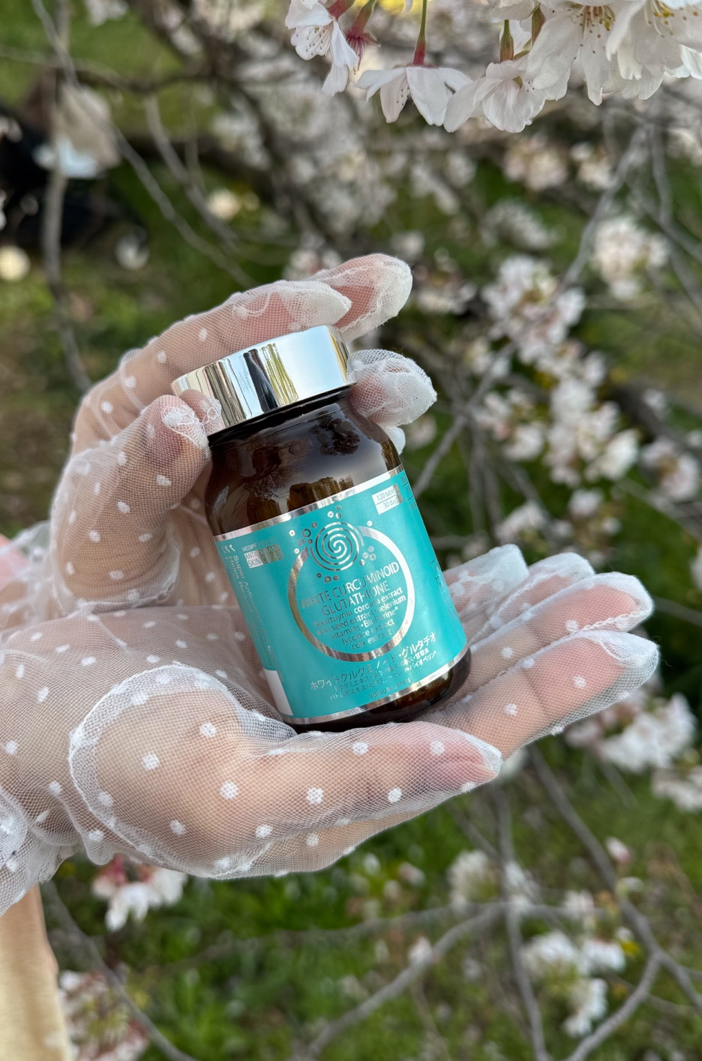 White Curcuminoid Glutathione bottle held beneath Japanese cherry blossom